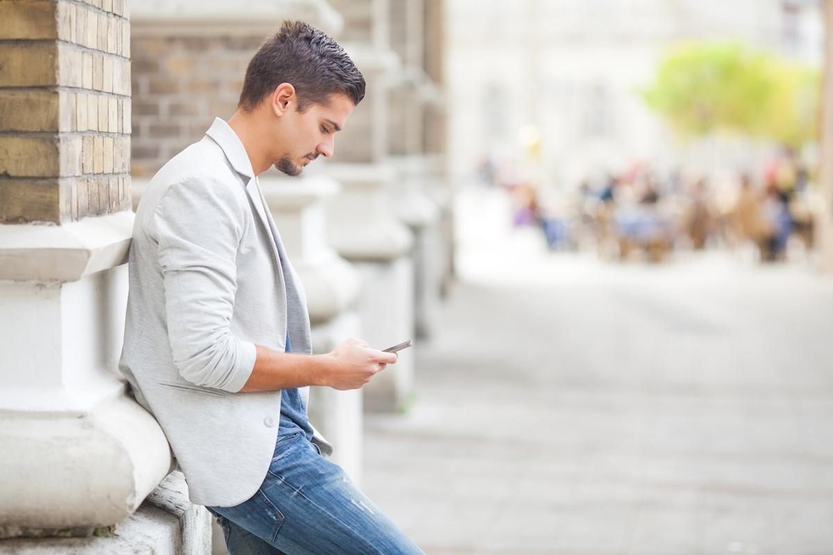 Man in jeans leans on building pillar while texting