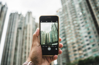 Man holding cell phone up and taking a low angle picture of a tall city skyline