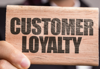 person holding a small piece of wood with the words "customer loyalty" printed on it