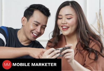 two people looking at a phone, Mobile marketer logo in the bottom left corner