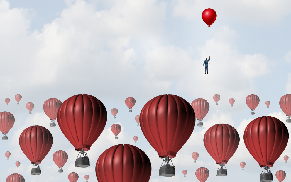 Businessman holding a red balloon and floating in the sky above hot air balloons